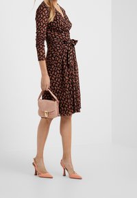 Svart omslagsklänning med orange och röd djurprint, rosa handväska med guldlås och persikofärgade högklackade skor med slingback-design.