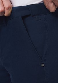 Granatowe spodnie z teksturowanej tkaniny, z zapięciem na guzik, akcentowanym pasem i detalem logo w pobliżu kieszeni.