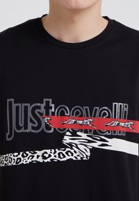 Camiseta de algodón negra con texto gris "Just Cavalli", con acentos gráficos rojos y estampados en prints de animales y formas estilizadas.