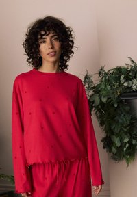 Piros loungewear szett, hosszú ujjú toppa, szívmintákkal és rugalmas derékkal. Puha anyag, laza szabású.