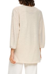 Béžová texturovaná pletená tunika se tříčtvrtečními rukávy, volným střihem a kulatým výstřihem, sahající do poloviny boků.