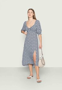 Vestido de estampado floral em azul marinho e branco, com mangas curtas em puff, decote profundo, fenda frontal e um tecido leve e fluido.