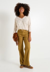 Pull léger beige avec de petits motifs en forme de cœur, associé à un pantalon large moutarde. Accessoirisé avec une pochette marron et des baskets noires à imprimé léopard.