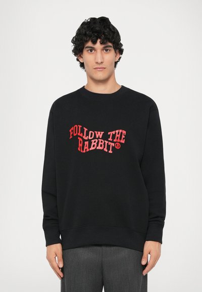Sweatshirt noir en coton, avec un texte graphique rouge "SUIVEZ LE LAPIN" dans un design ondulé. Encolure ronde, manches longues, poignets côtelés.