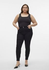 Svarta högmidjade jeans med en figurnära passform, som har framfickor, dubbelknäppning och matchas med en svart linne och klackar.