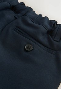 Marineblauwe stof short met een elastische tailleband, een zijzak en een zwarte knop met 'Clarks' erin gegraveerd. Gladde textuur.
