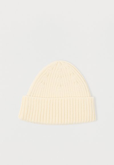 Πλεκτό σκουφάκι σε κρεμ απόχρωση, με ριμπ σχέδιο και αναδιπλούμενη μανσέτα. Το υλικό φαίνεται μαλακό με υφασμάτινη υφή, κατάλληλο για κρύο καιρό.