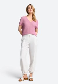 Rosa gestricktes V-Ausschnitt-Top mit kurzen Ärmeln, kombiniert mit weißen, taillierten Hosen mit elastischen Bündchen und Zugbändern, getragen mit weißen Sandalen.