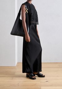 Czarna koronkowa bluzka na krótki rękaw z falbaniastymi krawędziami w połączeniu z długą czarną satynową spódnicą. Całość dopełnia czarna skórzana torebka na ramię oraz masywne klapki na otwartym palcu.