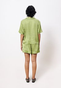 Satin-grünes Kurzarmhemd und passende Shorts, mit einem lockeren Schnitt und glatter Textur. Leopardenmuster-Schuhe ergänzen das Outfit.