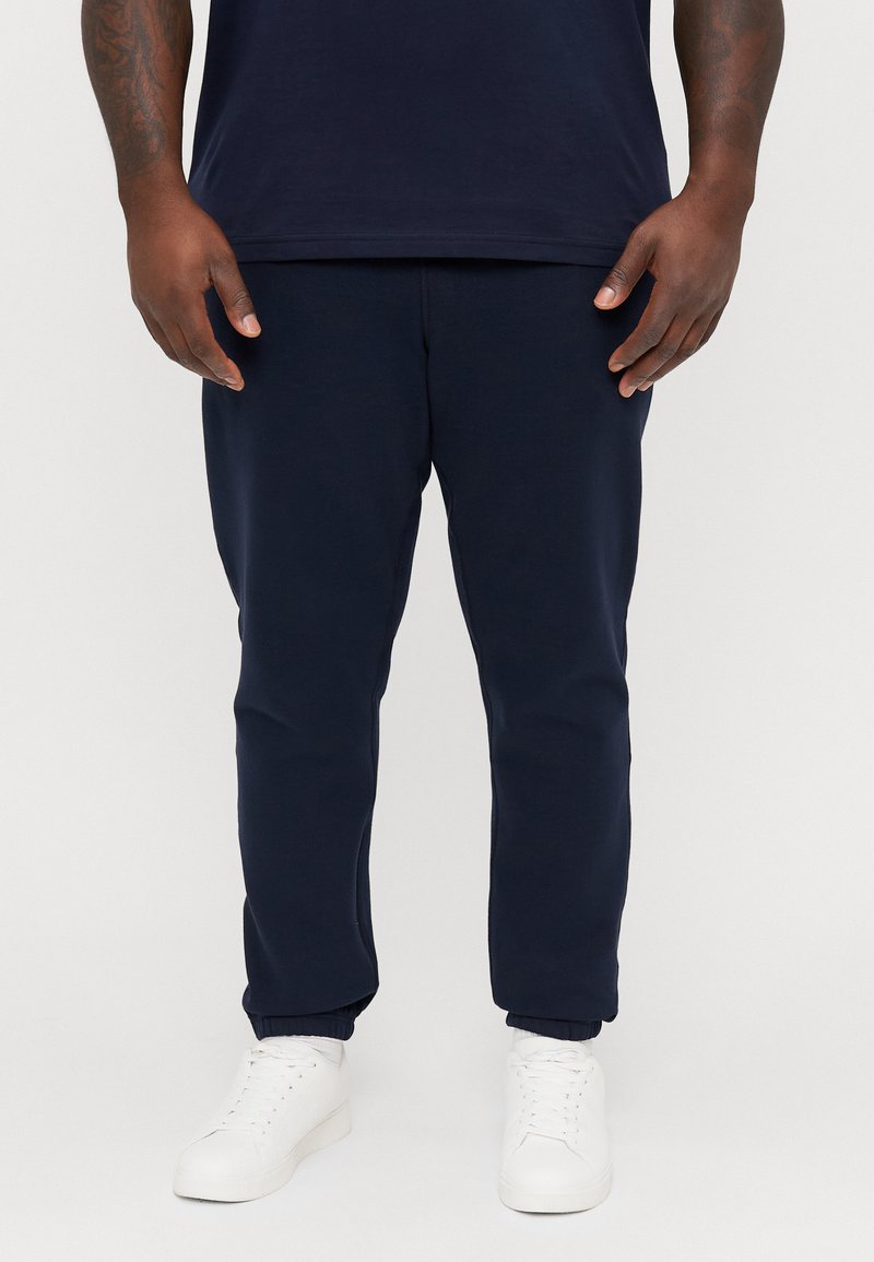 Granatowe dresy wykonane z miękkiego materiału, z elastycznymi mankietami i bocznymi kieszeniami, w połączeniu z białymi butami sportowymi.