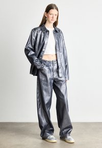 Metalizuotas sidabro marškinėliai ir platūs kelniai, pagaminti iš blizgaus audinio. Marškiniai turi spaudimo mygtukus, o kelnės pasižymi priekinėmis kišenėmis ir laisvu sijonu.