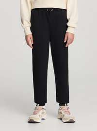 Pantaloni jogger neri elasticizzati con vita regolabile a coulisse. Design a gamba affusolata, tessuto morbido. Abbinati a sneakers beige e rosa.