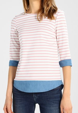 Mujer que lleva una camisa de rayas blancas y rosas con puños y dobladillo vaqueros, combinada con vaqueros azul oscuro.