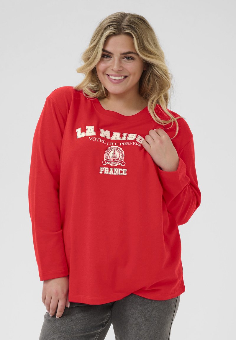 T-shirt rouge à manches longues avec un col rond, arborant le texte blanc "LA MAISON" et des graphiques. Tissu doux avec une coupe décontractée.