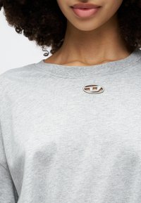Sweatshirt cinza de mangas curtas com um detalhe em logo prateado redondo no decote, feito de um tecido suave e texturizado.