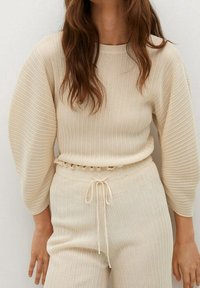 Pull en tricot beige avec de longues manches bouffantes et un col rond, associé à un pantalon léger à taille élastique assorti en texture côtelée.