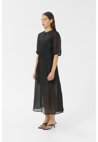 Black, sheer midi dress with short sleeves, button front, and vertical pleats. Paired with black, minimalistic heeled sandals.