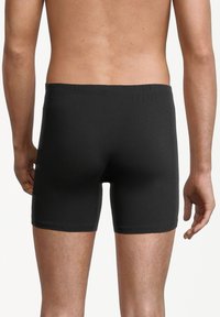 Uomo che indossa boxer aderenti neri semplici, visto da dietro su uno sfondo bianco.