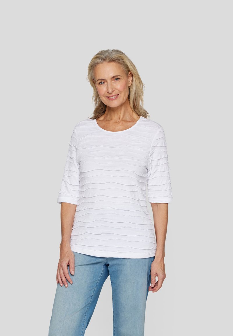 Weißes T-Shirt mit strukturierten, wellenförmigen Mustern, rundem Ausschnitt und Dreiviertelärmeln, kombiniert mit hellblauen Jeans.