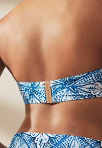 Bikini-yliosa, jossa on sinivalkoinen kukkakuosi, sileä kangas, joustava nauha ja kultainen kiinnitys takana.