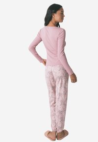 Top a maniche lunghe rosa abbinato a pantaloni da pigiama floreali rosa chiaro, con una texture morbida e un elastico in vita. Morbide pantofole completano il look.