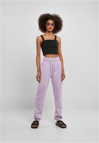 Débardeur noir coupé, pantalon de survêtement lavande avec cordon de serrage, sandales plates noires et lunettes de soleil violettes. Texture lisse, coupe décontractée.