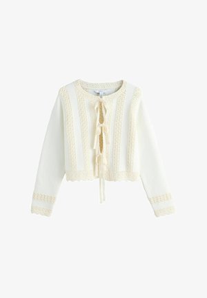 Krämfärgad stickad kofta med långa ärmar, texturerade vertikala ränder, scalloped kanter och tre rosetter framtill på vit bakgrund.