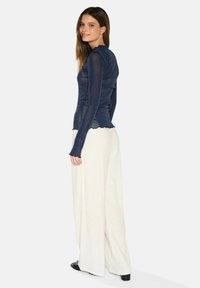 Marinblå långärmad topp med en figurnära design och scallopkanter. Matchad med krämfärgade vida byxor och svarta skor. Strukturerad tyg.