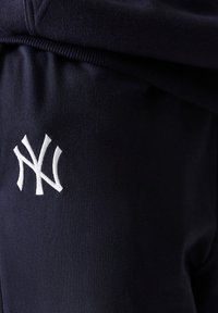 Marineblå joggingbukser med en blød tekstur, prydet med et hvidt broderet logo på venstre side og et ribbet taljebånd.