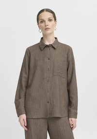 Chemise marron à boutons avec un motif texturé et ray�é, dotée d'une poche sur la poitrine, de manches longues et d'un col classique.