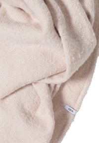 Měkká, světle béžová texturovaná látka složená s malou bílou visačkou s nápisem "CECIL" viditelnou blízko okraje.