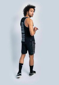 Top sportivo nero a maniche corte e pantaloni corti con la scritta "BIDI BADU" stampata in grigio. Presenta scollature basse, un collo rotondo e sneaker nere.