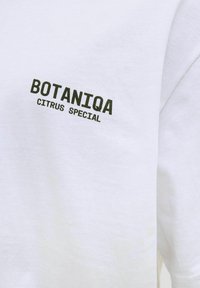 Hvid bomulds T-shirt med sort trykt tekst "BOTANIQA" og "CITRUS SPECIAL" på venstre bryst. Simpelt design med en blød tekstur.