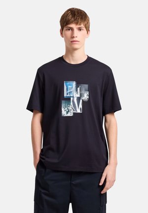 Sort bomulds t-shirt med et grafisk design bestående af fire billeder i nuancer af blå og sort, der viser bylandskaber og arkitektur.