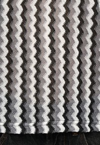 Ύφασμα με ρίγες σε ζιγκ-ζαγκ σε εναλλασσόμενες αποχρώσεις λευκού, γκρι και μαύρου, με ορατή ραφή κατά μήκος του κάτω μέρους πάνω από σκουρόχρωμο υλικό τζιν.