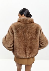 Brun faux fur cropped jakke med høj krave, brede ærmer og en blød tekstur, vist fra ryggen mod en lys baggrund.