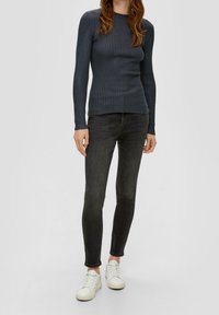 Dunkel gerippter Langarmoberteil kombiniert mit schwarzen Skinny Jeans und weißen Sneakern. Das Oberteil hat einen runden Halsausschnitt und eine figurbetonte Passform.