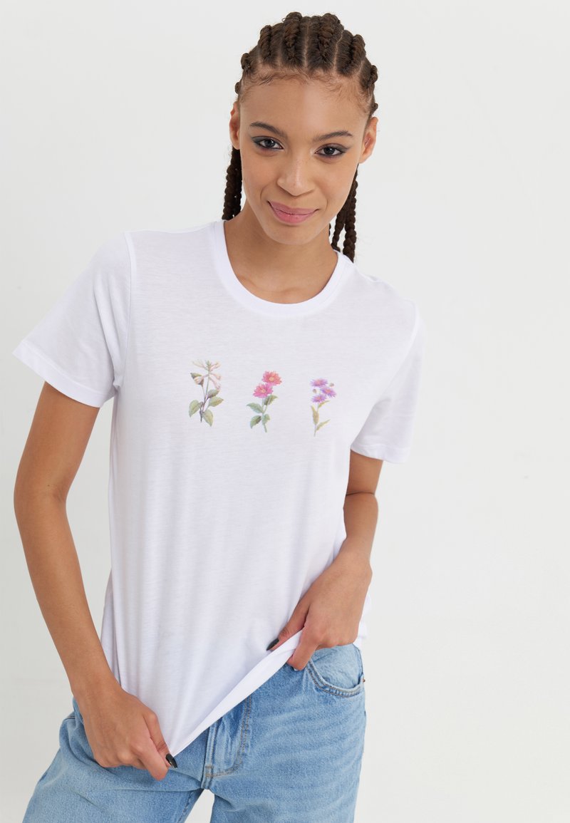 Witte t-shirt met korte mouwen, versierd met drie geborduurde bloemen in pastelkleuren. Ontspannen pasvorm met een ronde hals en een zachte stofstructuur.