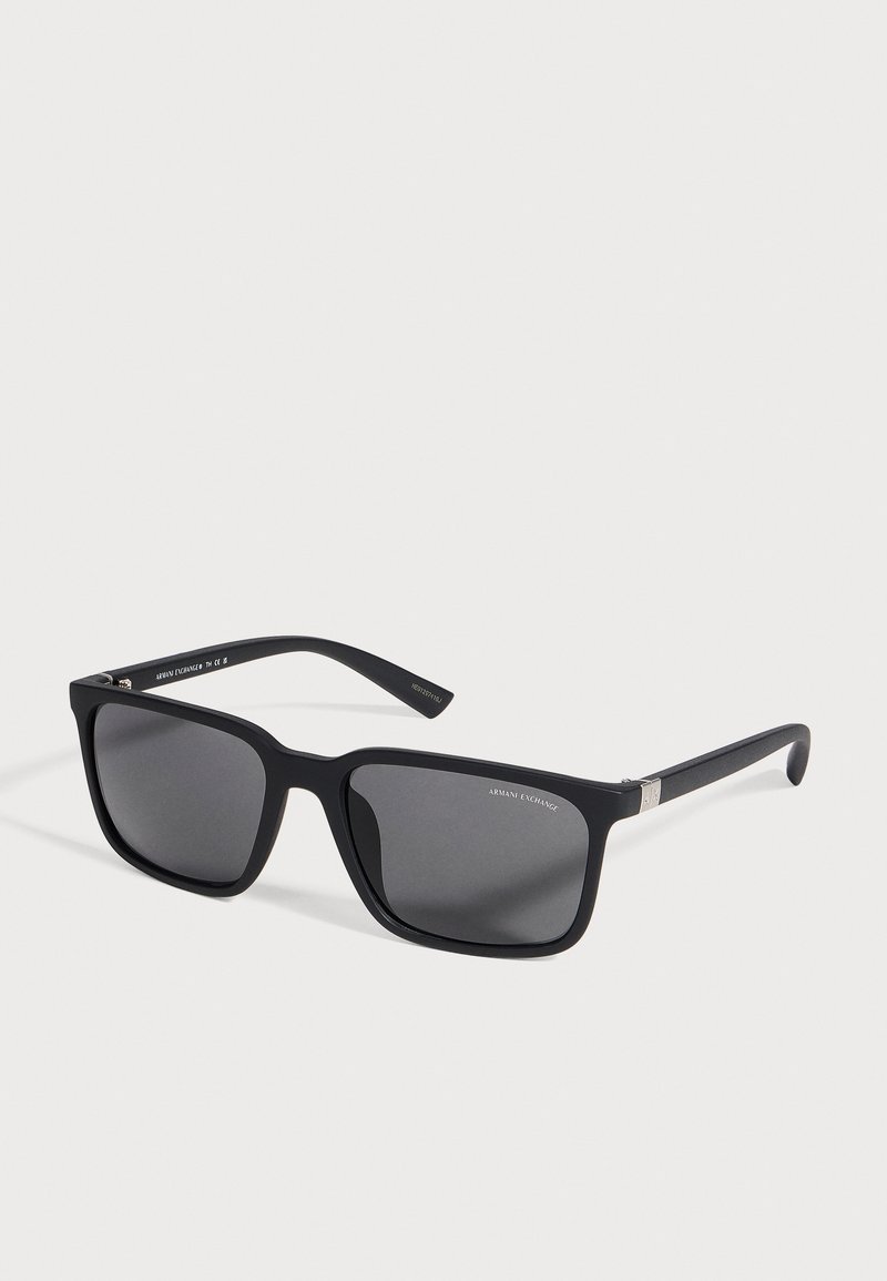 Lunettes de soleil noires Armani Exchange à monture rectangulaire, avec des verres gris foncé et des accents argentés au niveau des charnières, sur un fond clair.