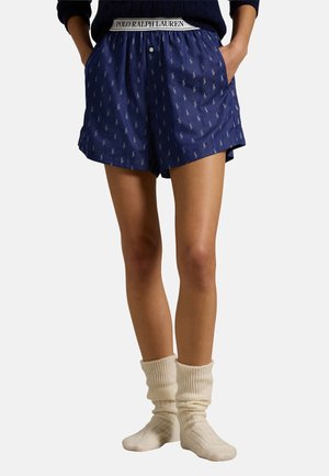 Blaue Baumwollshorts mit einem sich wiederholenden hellblauen Logo-Muster, ausgestattet mit einem elastischen Bund mit dem Schriftzug "POLO RALPH LAUREN". Kombiniert mit weißen, gerippten Socken.