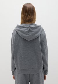 Grijze sweatshirt met een capuchon, met een ontspannen pasvorm, geribbelde mouwen en zoom. Zachte textuur, minimaal ontwerp, gezien vanaf de achterkant.