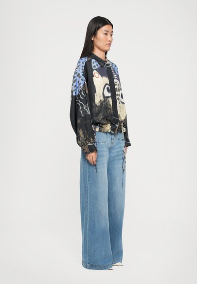 Black, patterned blouse with blue and gold graphics, paired with wide-leg light blue jeans featuring a relaxed fit and subtle detailing.