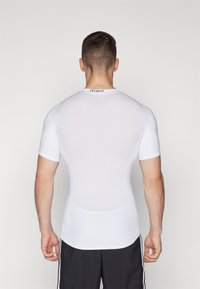 Vit kortärmad träningsskjorta med en åtsittande design, slät yta och en liten "TECHFIT"-etikett vid halsringningen.