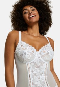 Lingerie en dentelle blanche avec des panneaux en mesh transparent, motifs floraux, bretelles ajustables et un détail en trou de serrure au centre devant.