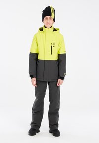 Veste d'hiver jaune et grise avec poches zippées, accompagnée de pantalons gris. Bonnet en tricot noir avec accents de logo. Tissu lisse et durable.