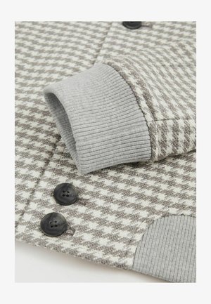 Tessuto a motivo houndstooth grigio e crema con polsini a coste, caratterizzato da due bottoni neri, cuciture dettagliate e variazioni di texture.