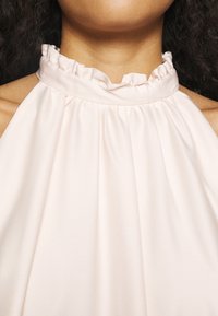 Mujer que lleva un top halter de color rosa pálido con un escote fruncido y con volantes, mostrando sus hombros y la parte superior del pecho.