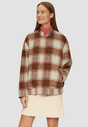 Bruine en witte geruite fleece pullover met een hoge kraag, lange mouwen en vo pockets, gecombineerd met een lichtbeige rok.