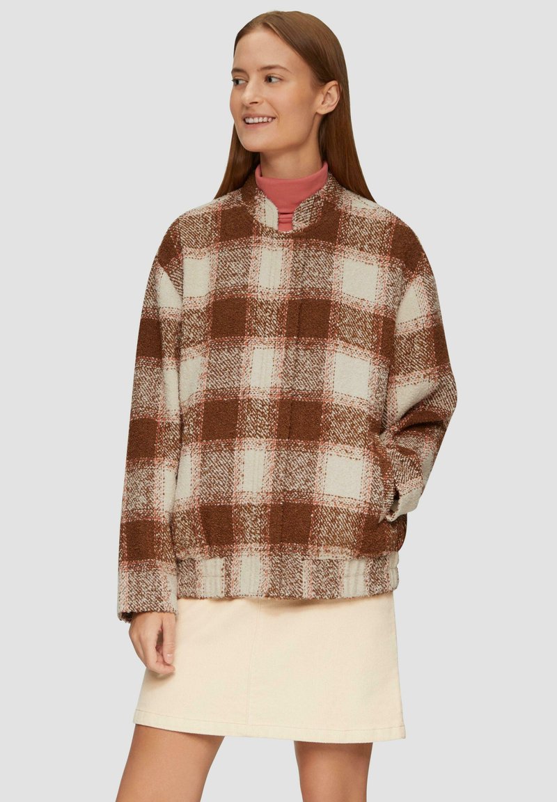 Bruine en witte geruite fleece pullover met een hoge kraag, lange mouwen en vo pockets, gecombineerd met een lichtbeige rok.